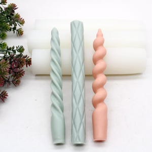 May include: Three candle molds made of silicone. The molds are in the shape of a spiral, a diamond pattern, and a twisted rope. The molds are light green and pink.
