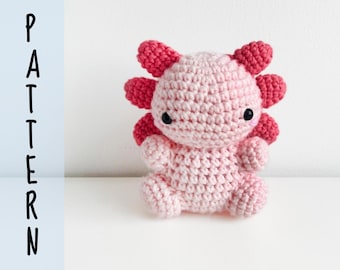 May include: A light pink crocheted axolotl plush toy with dark pink external gills, small black eyes, and a rounded body. The word PATTERN is printed vertically in black sans-serif letters on the left side of the image against a light blue bar.