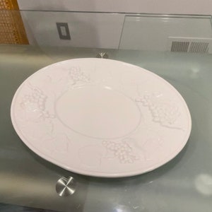 Puede incluir: Plato de servir de cerámica blanca con un diseño en relieve de uvas y hojas alrededor del borde.