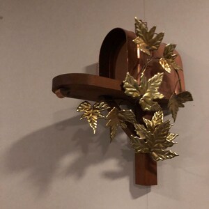 May include: A copper mailbox with a wooden base and gold leaf accents. The mailbox is decorated with a vine of gold leaves.