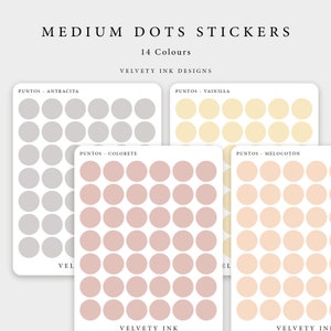 Puede incluir: Una colección de pegatinas de puntos medianos en varios colores, incluyendo gris, amarillo pálido, melocotón y rosa. El texto en las pegatinas dice "MEDIUM DOTS STICKERS" y "14 Colores". La marca "VELVETY INK DESIGNS" también es visible.