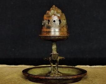 May include: A small, antique bronze incense burner with a decorative top and a round base. The burner has a traditional design with intricate details.