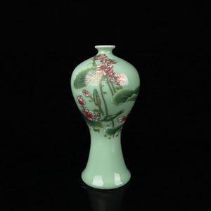 Könnte beinhalten: Eine hell mintgrüne Keramikvase mit engem Hals und ausgestelltem Fuß. Die Oberfläche zeigt ein gemaltes Design aus rosa Lotusblüten und dunkelgrünen Seerosenblättern mit goldfarbenen Umrandungen, was ein detailliertes botanisches Muster ergibt.