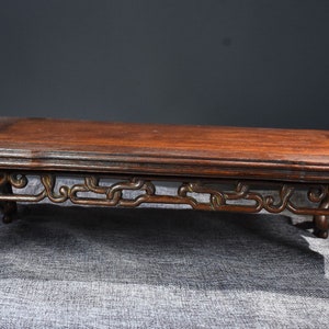 Pu&ograve; includere: Un tavolo in legno marrone scuro con intagli intricati sulle gambe e un piano rettangolare. Il tavolo &egrave; su una superficie di tessuto grigio.