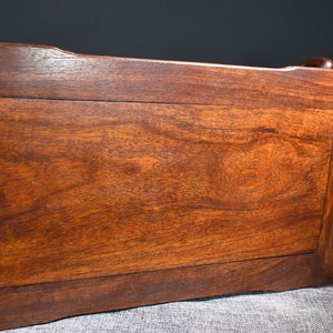Pu&ograve; includere: Il lato inferiore di un tavolo in legno marrone scuro con un piano rettangolare e un bordo leggermente rialzato. Il tavolo ha una superficie liscia e lucida.