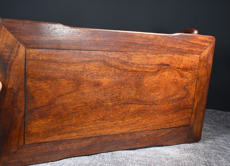 Pu&ograve; includere: Il lato inferiore di un tavolo in legno marrone scuro con un piano rettangolare e un bordo leggermente rialzato. Il tavolo ha una superficie liscia e lucida.