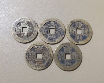 May include: Five antique Chinese coins with a square hole in the center and Chinese characters on the front. The coins are made of brass and have a worn, aged appearance.