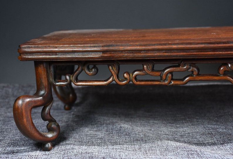 Pu&ograve; includere: Un supporto in legno marrone scuro con intagli intricati sulle gambe e un piano superiore piatto. Il supporto &egrave; in legno massello e presenta un design cinese tradizionale.