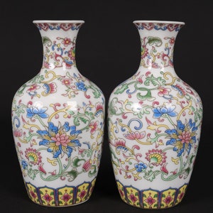 May include: A pair of white porcelain vases with a floral design. The vases feature a yellow, red, and blue floral pattern with green leaves. The vases have a yellow, red, and blue border at the bottom.