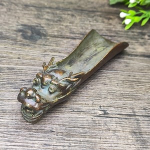 May include: A bronze dragon head incense burner with a long, narrow body. The dragon's head is detailed with scales and horns, and its eyes are inlaid with green stones.