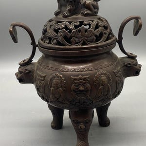 Op de afbeelding: Bronzen wierookbrander met ingewikkelde gravures. Het deksel heeft een beeld van een beschermende leeuw. De behuizing van de brander heeft reliëfsnijwerk van figuren en gezichten. De brander heeft drie poten en twee handvatten.