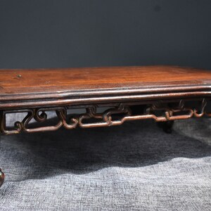 Pu&ograve; includere: Un tavolo in legno marrone scuro con intagli intricati sulle gambe e un piano rettangolare semplice. Il tavolo &egrave; su una superficie di tessuto marrone.