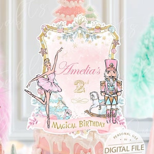 Könnte beinhalten: Ein rosa-weißer Tortendekor mit einer Ballerina, einem Nussknacker und einem Schaukelpferd. Der Dekor hat einen goldenen Rahmen und den Text "Amelia's 2nd Magical Birthday".