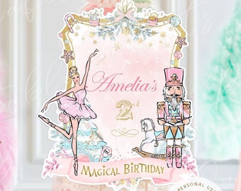 May include: A pink and white cake topper featuring a ballerina, a nutcracker, and a rocking horse. The topper has a gold frame and the text "Amelia's 2nd Magical Birthday".