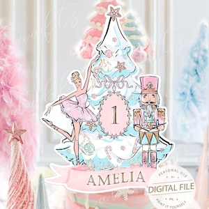 May include: A cake topper with a ballerina, a nutcracker, and a Christmas tree design. The topper is light blue and pink, with the name "AMELIA" on a banner. The cake is decorated with snowflakes and colorful sprinkles. The text "DIGITAL FILE" is also visible.