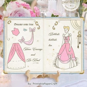 Puede incluir: Un decorado de libro de costura imprimible con Cenicienta en su icónico vestido de baile. El libro mide 26,7 cm por 38,1 cm e incluye un patrón para el vestido y una cita sobre tener coraje y ser amable.
