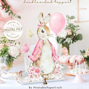 May include: A printable, double-sided cake topper featuring a watercolor illustration of a bunny holding a pink balloon. The bunny is wearing a pink jacket and a bow. The topper is surrounded by pink flowers and butterflies. The text "Bunny doublesided topper" is written in gold lettering above the bunny. The text "PERSONAL USE ONLY DIGITAL FILE PRINT IT YOURSELF" is written in a circle around the bunny.
