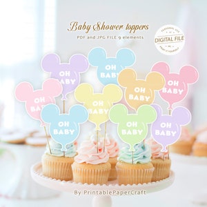 May include: Nine pastel-colored Mickey Mouse head shaped balloon cupcake toppers with the text "Oh Baby" in white. The toppers are on cupcakes with pastel frosting.