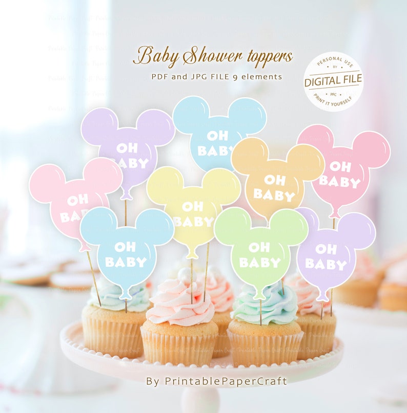 May include: Nine pastel-colored Mickey Mouse head shaped balloon cupcake toppers with the text "Oh Baby" in white. The toppers are on cupcakes with pastel frosting.