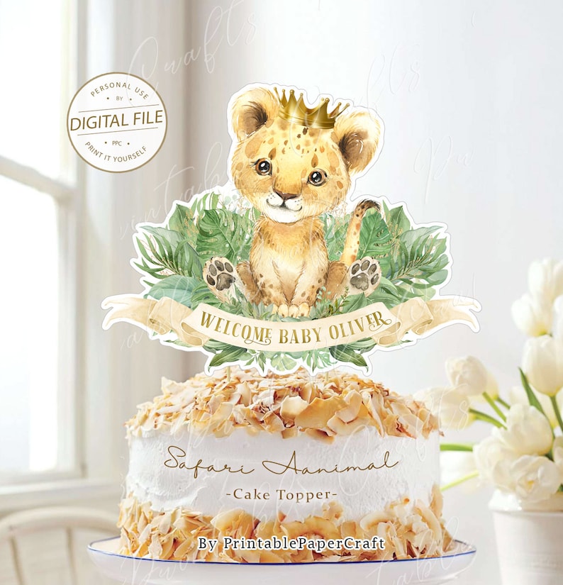 May include: A printable cake topper featuring a cute cartoon lion cub wearing a gold crown, surrounded by green leaves. The topper says "Welcome Baby Oliver" and "Safari Animal - Cake Topper - By PrintablePaperCraft".