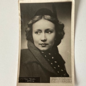 Może przedstawiać: Czarno-białe zdjęcie vintage kobiety z krótkimi, falującymi włosami, która nosi ciemny szal z białym wzorem. Zdjęcie jest pocztówką z tekstem "СОТО-ТРУД Гомель ЦЕНА 1р" i "НАРОДНАЯ АРТ» РОВЕРЬ КАЗНОО Г-С-УЛАНОВА" wydrukowanym na dole.