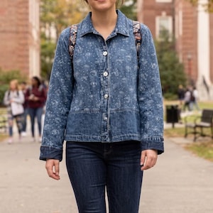 May include: A blue denim jacket featuring a white paisley and dot pattern, a classic collar, long sleeves, and a button-down front closure. The jacket has a horizontal seam across the midsection and is paired with dark blue denim jeans.