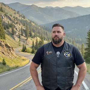 May include: A black leather vest featuring a V-neckline, front snap buttons, and side lacing. The vest is adorned with a small eagle pin on the right chest and a circular yellow and blue patch with text on the left chest over a black t-shirt.