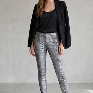 May include: A black blazer worn over a black v-neck camisole and silver snakeskin-patterned skinny pants. The outfit is completed with black leather ankle boots. The ensemble features a structured jacket, a smooth top, and textured trousers.