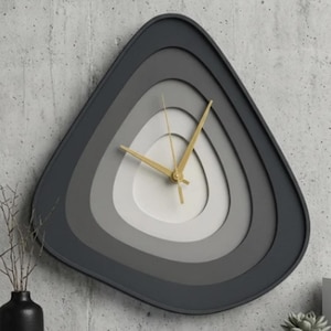 May include: A modern, layered wall clock in a triangular shape. The clock face features concentric layers of gray and white, with gold-colored hands. The clock is mounted on a textured gray wall, creating a minimalist aesthetic.