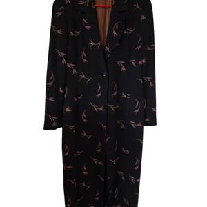 May include: A long black coat featuring a repeating pattern of small, light brown tulip-like floral motifs. The coat has a notched lapel, long sleeves, a single front button closure, and a brown interior lining visible at the collar area.