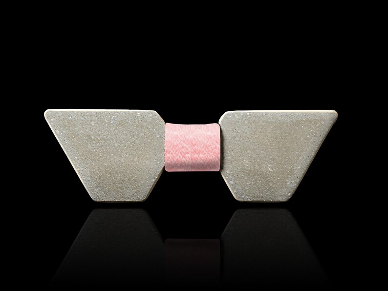 May include: A grey bow tie with a pink bow in the centre. The bow tie is made of a textured material.
