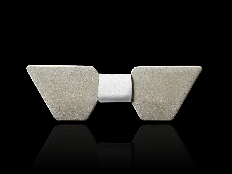 May include: A grey concrete bow tie with a white fabric centre. The bow tie is a modern and minimalist design.