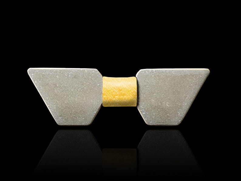 May include: A silver bow tie with a yellow centre. The bow tie is made of two triangular pieces of metal.