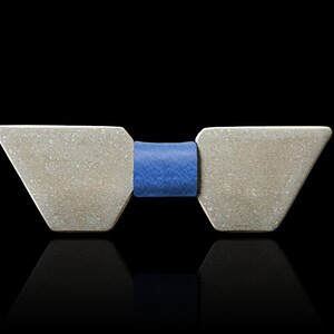 May include: A silver bow tie with a blue band in the centre. The bow tie is made of two triangular pieces.