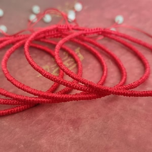 May include: A stack of red string bracelets, each with a small white bead at the end.