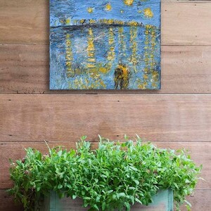 Puede incluir: Una pintura abstracta azul y dorada con un cielo nocturno estrellado y un reflejo de las estrellas en el agua debajo. La pintura est&aacute; enmarcada y colgada en una pared de madera.