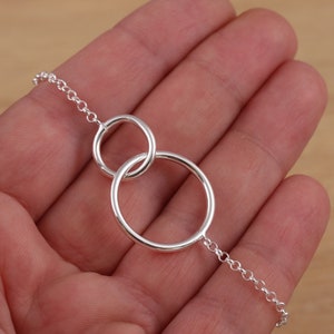 May include: A silver chain necklace with two interlocking circles. The circles are connected by a delicate chain.