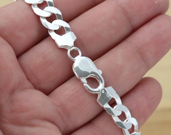 May include: A silver curb chain bracelet with a lobster clasp. The bracelet features a series of interconnected, flattened oval links. The clasp is a secure, polished metal component. The bracelet is shown against a neutral background.