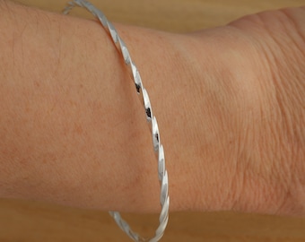 May include: A silver twisted bangle bracelet. The bracelet is made from a single piece of metal that is twisted into a spiral shape.