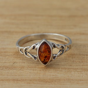 Op de afbeelding: Een zilveren ring met een marigold amber edelsteen gezet in een Keltisch knoopontwerp.