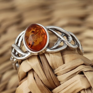 Op de afbeelding: Een zilveren ring met een Keltisch knoopontwerp en een barnsteen.