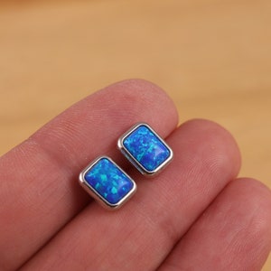 Puede incluir: Un par de pendientes de plata con piedras de ópalo azul. Las piedras son rectangulares y tienen un acabado brillante e iridiscente.