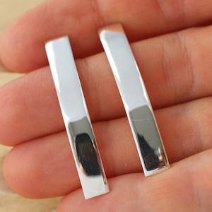 May include: A pair of silver bar earrings. The earrings are long and narrow, with a smooth, polished finish.