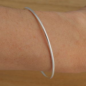 May include: A simple silver bangle bracelet, worn on a person's wrist.