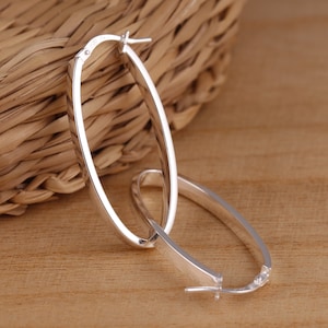 Puede incluir: Un par de pendientes de aro ovalados de plata. Los pendientes son simples y elegantes, y serían una gran adición a cualquier colección de joyas.