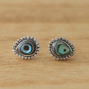 Op de afbeelding: Een paar zilveren oorbelletjes met een traanvormige inleg van abalone-schelp. De schelp heeft een blauwe, groene en iriserende glans.
