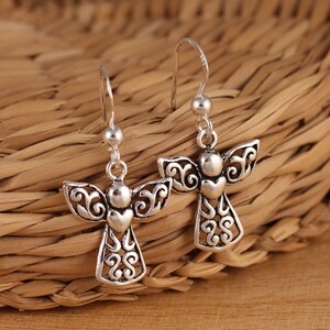 May include: A pair of silver dangle earrings featuring an angel design with intricate details. The angel has a heart-shaped body and delicate wings.