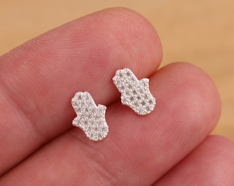 May include: A pair of silver earrings in the shape of a hamsa hand, each hand is covered in small, clear cubic zirconia stones.