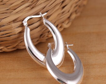 May include: A pair of silver hoop earrings with a smooth, oval shape. The earrings are simple and elegant.