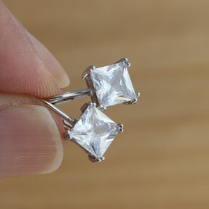 May include: A pair of silver earrings with square-shaped clear cubic zirconia stones.